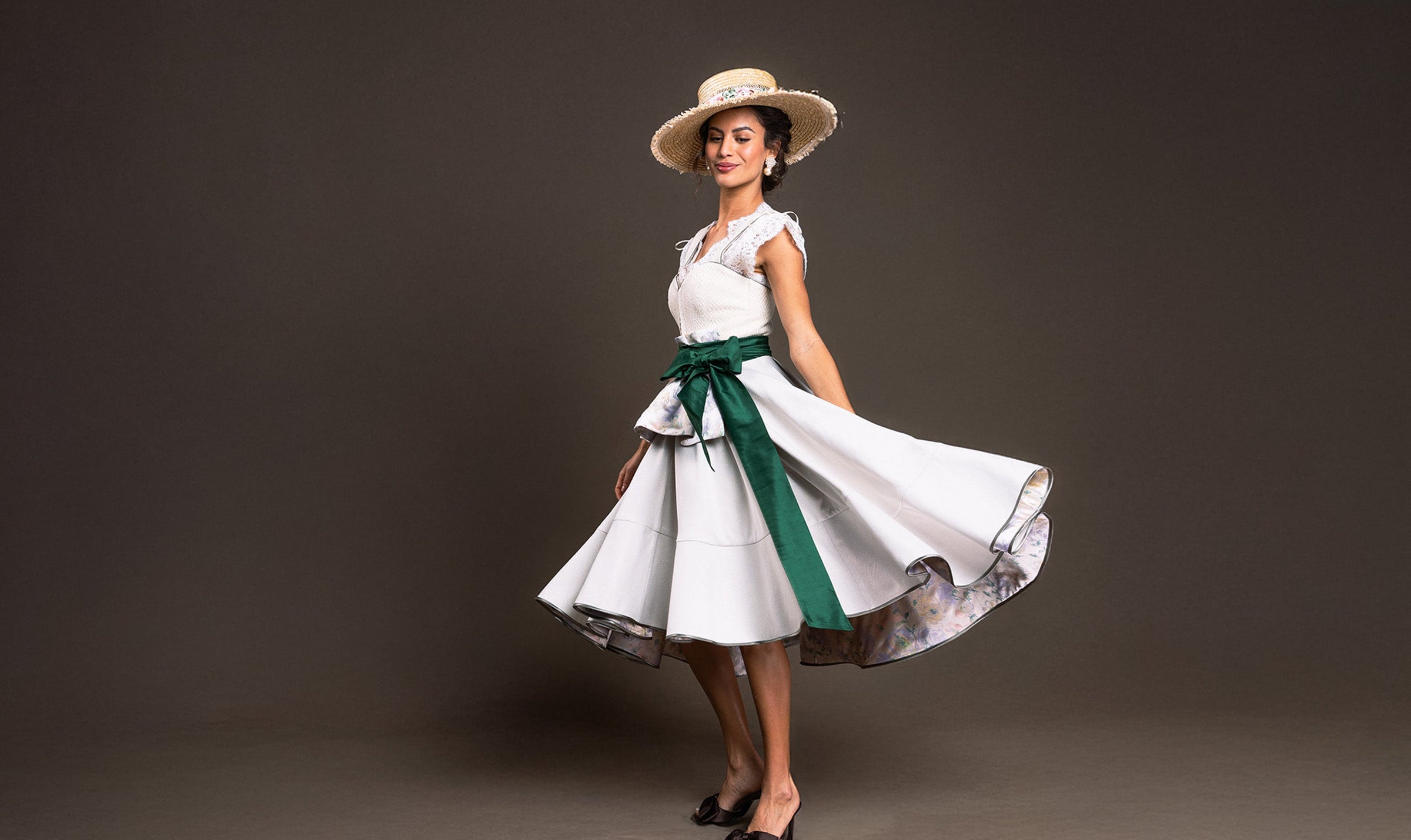 Elegantes Designer-Dirndl in Weiß mit grüner Schleife und Strohhut – modernes Dirndl von Policarpo Trachten
