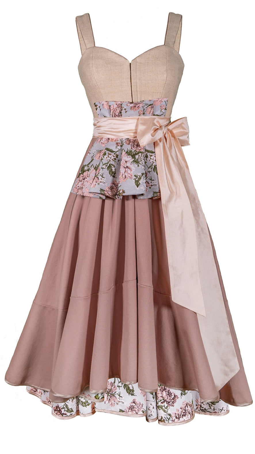 Ein freigestelltes Dirndlkleid in rosa Cremetönen mit einem Schösschen aus Blumenstoff vorne gebunden mit einer hellrosa Schleife. Das Dirndl hat ein weit ausgestellten Rock und auf der Innenseite des Saums ebenfalls Florale Muster