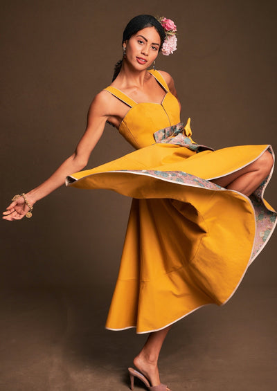 ein Sonnengelbes Kleid mit Schürzchen um die Taille mit einem tanzenden Rockschwung präsentiert
