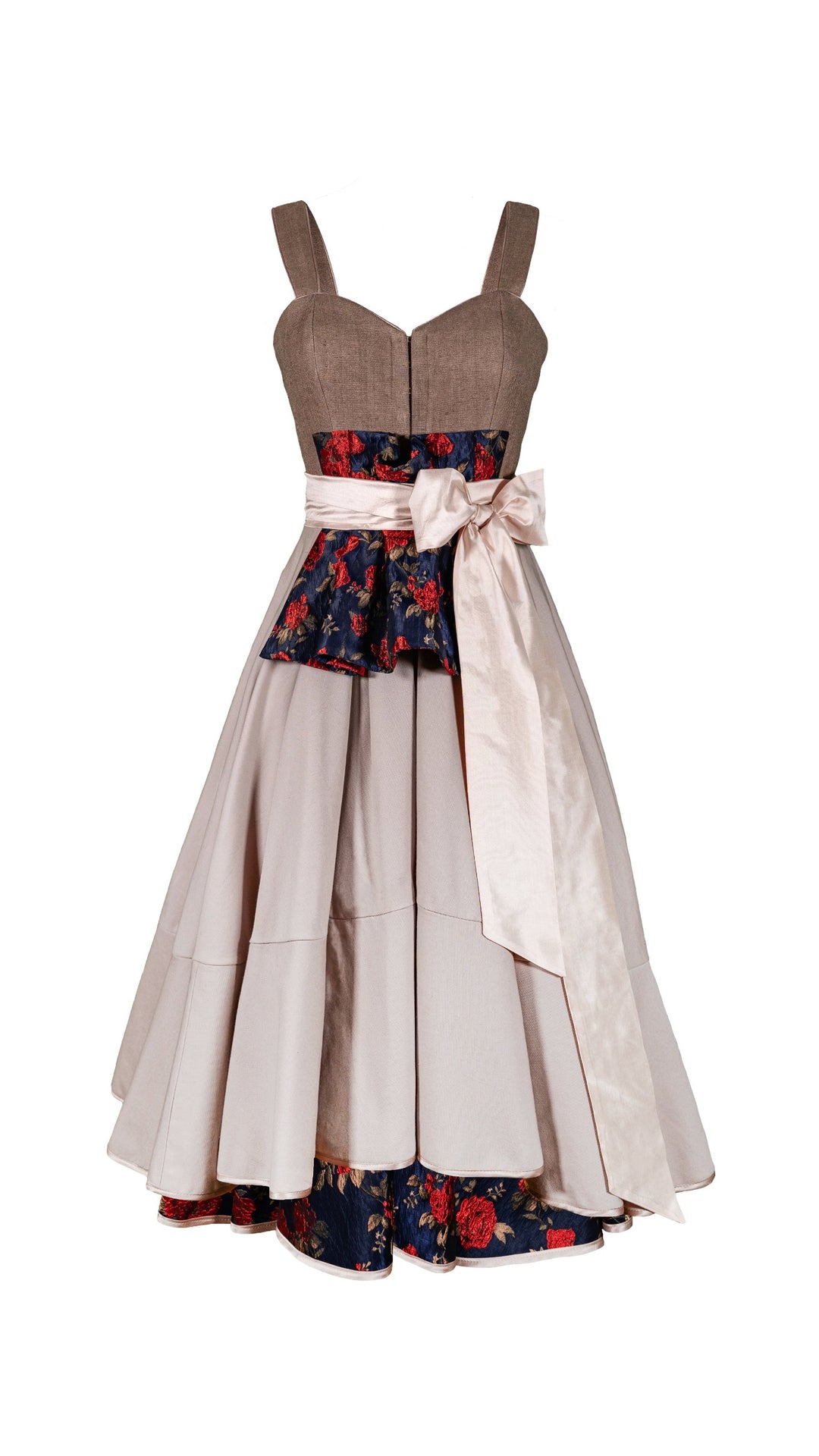 Ein Dirndl auf weissem Hintergrund ohne Schürze. Ein beigefarbenes Trachtenkleid mit einem stark tradierten Rockteil in Sand und floralen Mustern auf der kurzen Schürze unter dem Schleifenband geknöpft. Das Schleifenband in zartrosa in Seide. Das Mieder hat einen herzförmigen Ausschnitt und das Dirndl kann somit ohne Bluse wunderbar getragen werden. Auf der Rockinnenseite findet man den gleichen floralen JAcquardstoff wie beim Schösschen 