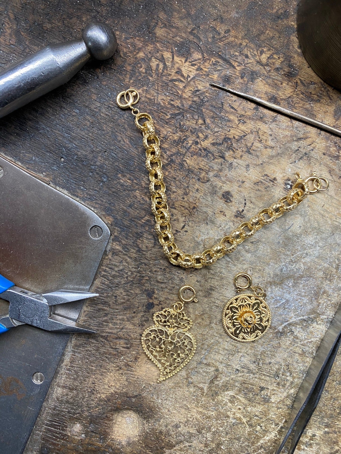 Das goldene Charivari liegt auf der Werkband der Produktion in Porto mit Werkzeugen daneben. Es ist in gelöst von den Anhängern und zeigt die Handarbeit und Filigrane aus liebe zur Tradition. and den Verschlüssen sind bereitgestellte Ringe zur Anbindung an das Policarpo Dirndl